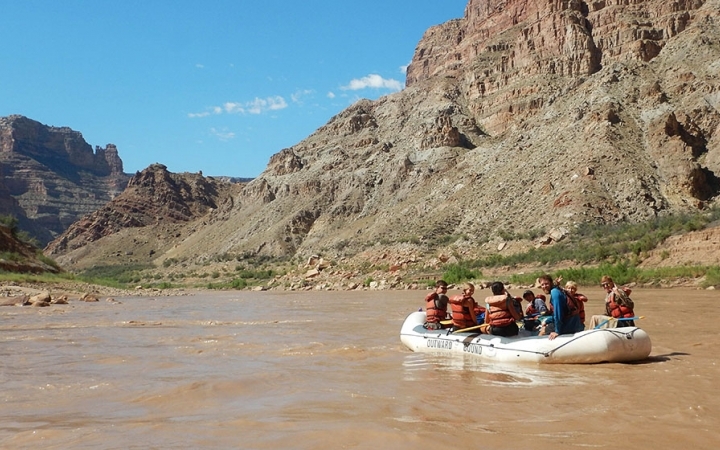 outward bound gap year students paddle a raft on a muddy river surrounded by high canyon walls